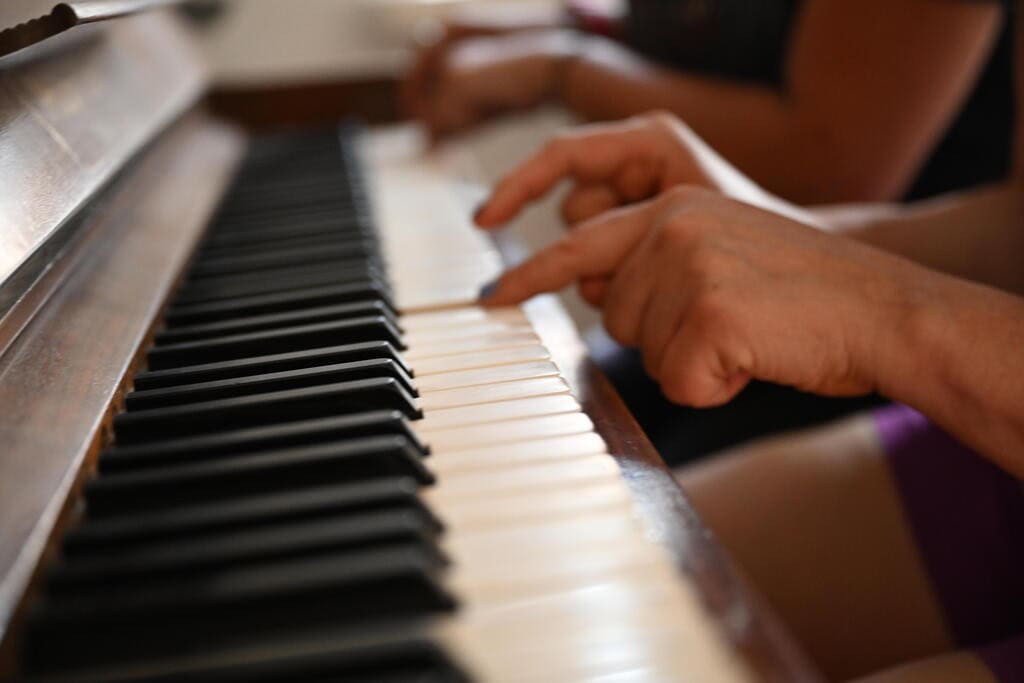 Nahaufnahme von zwei Händen, die Klavier spielen, weiße und schwarze Tasten, lichtdurchflutet.
