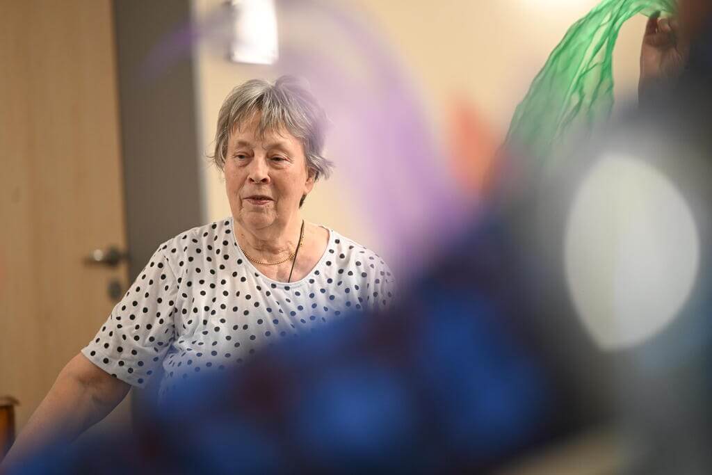 Ältere Frau mit grauen Haaren und gepunktetem Shirt schaut nachdenklich. Verschwommener Hintergrund.